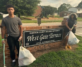 2024 Clean and Green. Two people with filled garbage bags standing by the West Gate Terrace sign.