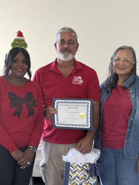 Luther Harrison smiling and holding his 20 year award.