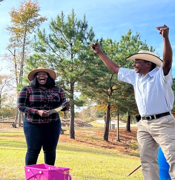 James Currie smiling with his hands up in the air, with a woman smiling next to him.